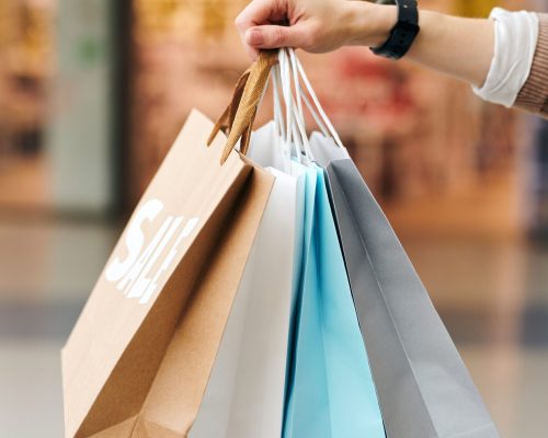 Close-up of unrecognizable woman holding heap of shopping bags in mall